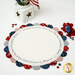 A round hand embroidered table topper with a scalloped edge in red, white, and blue fabrics from the American Gatherings III collection by Moda, featuring the Pledge of Allegiance stitched in the center.