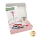 The open May box containing colorful embroidery floss, a pattern card, and needle minder, all on a bed of white raffia.