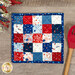 The completed Fusible Grid Hot Pad colored in red, blue, and white fabrics from the Firecracker collection by Riley Blake Designs. The project is staged on a wood table where a wooden spoon and patriotic garland peek into frame.