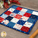 An angled shot of the finished hot pad, showing details on the patriotic fabrics. Coordinating utensils and décor peek into frame from either side.