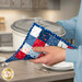 A model uses the hot pad to carry a white ceramic dish. Coordinating décor can be seen in the background.