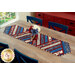 The completed Greased Lightning Table Runner in red, white, and blue fabrics from the Stars & Stripes 14 collection by Northcott Fabrics, staged on a rustic wood table with flowers.