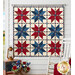 The completed Vintage Stars Quilt, colored in red, cream, and blue fabrics from the American Heartland collection Northcott Fabrics, hung on a white paneled wall on a porch and staged with coordinating décor.