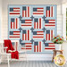 The completed God and Country Quilt featuring alternating red, white, and blue fabrics from the Independence Day collection from Moda Fabrics hangs on a porch, with a chair and flowers nearby.