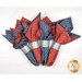 Four folded napkins in red and blue patterns with silver bands resting on a white surface.