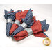 Four folded napkins in red and blue patterns with silver bands resting on a white surface.