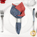 A top down shot of the napkin with the blue fabric faced out, staged on a white table setting with silverware and a glass.