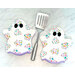 Two of the ghostly hot pads in white fabrics with multicolor ghosts, staged with a spatula.