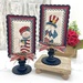 The two completed cross stitch projects of Sam and Betsy, set on parchment cream fabric and stitched with rustic colors, displayed on a Paisleys and Polka Dots mount.