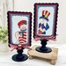 The two completed cross stitch projects of Sam and Betsy, set on light blue fabric and stitched with bright colors, displayed on a Paisleys and Polka Dots mount.