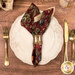 A top down shot of the napkin with the red floral side out; the napkin is staged with a white plate, silverware, and matching cup.