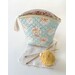 A shot of one of the big pouches, colored in pastel prints and staged with knitting needles and yarn.