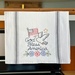 A decorative kitchen towel featuring the text God Bless America, an American flag, an eagle, and flowers.