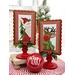 The two completed cross stitch projects of Santa & Rudolph, set on pale blue fabric and stitched with bright colors, displayed on a Paisleys and Polka Dots mount painted red and green.