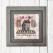 The framed cross stitch project featuring a house, stars, and the phrase One Nation Under God.