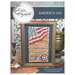 The front of the cross stitch pattern with the completed project framed and surrounded by coordinating décor. 