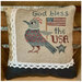 Completed cross stitch design as a pillow featuring a bird holding a flag and the words "God bless the USA."