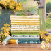 A stack of the fabrics included in the Buttercup & Blues collection, with flowers and jars and a vase and thread and a window.