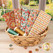 A stack of the Village Life - Rust & Ochre fat quarter bundle, with a basket and a window and a garden and buttons and thread.