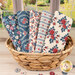 A stack of the Village Life - Blue Fat Quarter bundle, with a basket and a window and a garden and buttons.