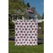 Quilt with red, white, and blue geometric patterns displayed in front of a white house and flag.