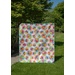A colorful, patterned fabric hung outdoors with bright geometric designs against a green backdrop.
