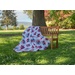 A colorful quilt draped over a wooden bench in a grassy park surrounded by trees.