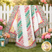 The completed 28th Floor Quilt colored in rich pink, aqua, chiffon yellow, and white fabrics from the Peony Blossoms collection by Wilmington Prints, artfully draped over a white picket fence and staged with coordinating flowers.
