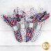Four folded napkins in red, white, and blue fabrics with silver bands resting on a white surface.