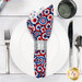 A top down shot of the napkin with the multi fabric faced out, staged on a white table setting with silverware and a glass.