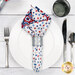 A top down shot of the napkin with the white starry fabric faced out, staged on a white table setting with silverware and a glass.
