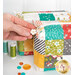 A model's hand shows details on the zipper pull charm; details on the fabric colors and prints can be seen.