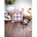 Decorative embroidered cushion on a wooden table, with a bowl of colorful buttons and yarn in the background.