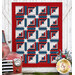The completed Steadfast Quilt, colored in red, white, and blue fabrics from the Seasonal Basics collection by Riley Blake Designs, staged on a white barn door wall and staged with flowers and a vintage red truck.