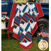 The completed Steadfast Quilt, colored in red, white, and blue fabrics from the Seasonal Basics collection by Riley Blake Designs, artfully draped over the bed of a vintage blue truck and staged with coordinating flowers and American flags.