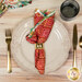 A top down shot of the napkin with the red side out, showcasing the geometric print; the napkin is staged with a cream plate and matching table setting.