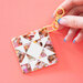 the quilt block bag charm on a pink background with a model holding the clasp. 