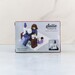 The back of the Sallie Tomato Sewist Building Block Set box, staged on a marble countertop and showcasing the completed set with the sewist at her sewing table.