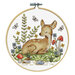 The completed cross stitch deer nestled among florals, butterflies, and mushrooms, framed in a wooden embroidery hoop.