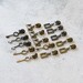 Assorted metal zipper pulls in antique, nickel, and gunmetal, displayed neatly on a white countertop.