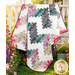 The completed Ridiculously Easy Jelly Roll Quilt colored in vibrant watercolor prints from the Soulstice collection by Moda Fabrics, artfully draped over a white fence and staged with coordinating flowers.