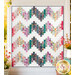 The completed Ridiculously Easy Jelly Roll Quilt colored in vibrant watercolor prints from the Soulstice collection by Moda Fabrics, staged on a white porch wall with coordinating flowers.