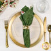 A top down shot of the napkin with the green fabric facing out, staged on a coordinating gold table setting on a white marbled
