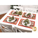 Lifestyle shot of a white dining table with the four Christmas-themed red placemats, coordinating plates, and folded napkins.