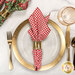 A top down shot of the napkin with the red gingham fabric facing out, staged on a coordinating gold table setting on a white marbled table.