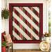 The completed 28th Floor Quilt colored in cream, red, pink, and green fabrics from the Hearth & Home collection by Henry Glass Fabrics, staged on an off-white porch wall with coordinating furniture and décor.