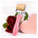 A pink-handled roller with a metal frame and a cylindrical wooden roller at the top styled with red roses and a pink heart with a white board and batten background.