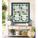 The completed Friendship Garden Wall Hanging, colored in white, navy blue, green, and yellow fabrics from the Friendship Garden collection by Henry Glass Fabrics, hung on a white porch wall and staged with coordinating flowers and décor.