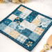 An angled shot of the finished hot pad, showing details on the blue and cream fabrics. Coordinating utensils and décor peek into frame from either side.