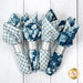 The four completed cloth napkins, colored in cream and blue fabrics from the Special Delivery collection by Andover Fabrics, staged on a white wooden table.